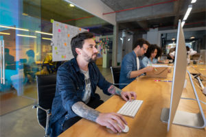 Man with tattoos using computer in shared office space