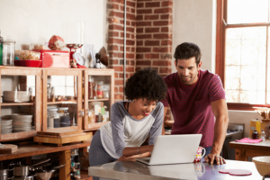 Young mixed race couple using computer in kitchen.