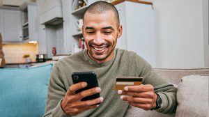 Man smiling while holding a credit card and phone