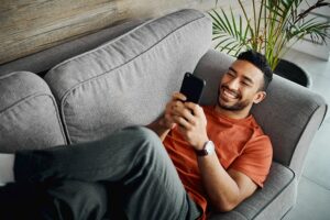 man smiling while using mobile phone on couch