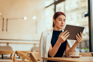 A focused woman working as a manager of the restaurant, using a digital tablet, and drinking coffee.