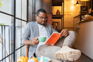 Man Reading At a Coffee Shop while holding a cup of coffee.