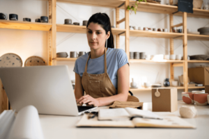 Female small business owner working on laptop from her modern pottery.