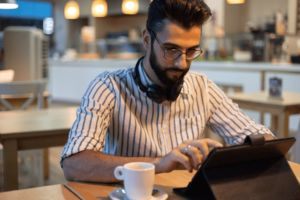 Handsome man with beard looking at tablet inside a bakery.