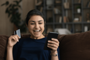 Excited young Indian woman shopping on cellphone at home.