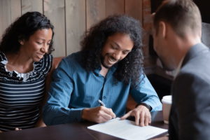 Millennial black spouses signing formal paper in presence of lawyer.