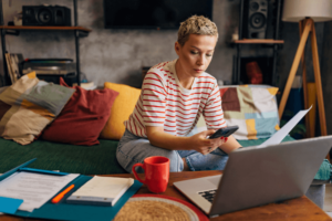 A woman manages her finances from home using a laptop and a mobile phone.