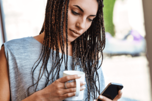 Young woman using smartphone while drinking coffee at home.